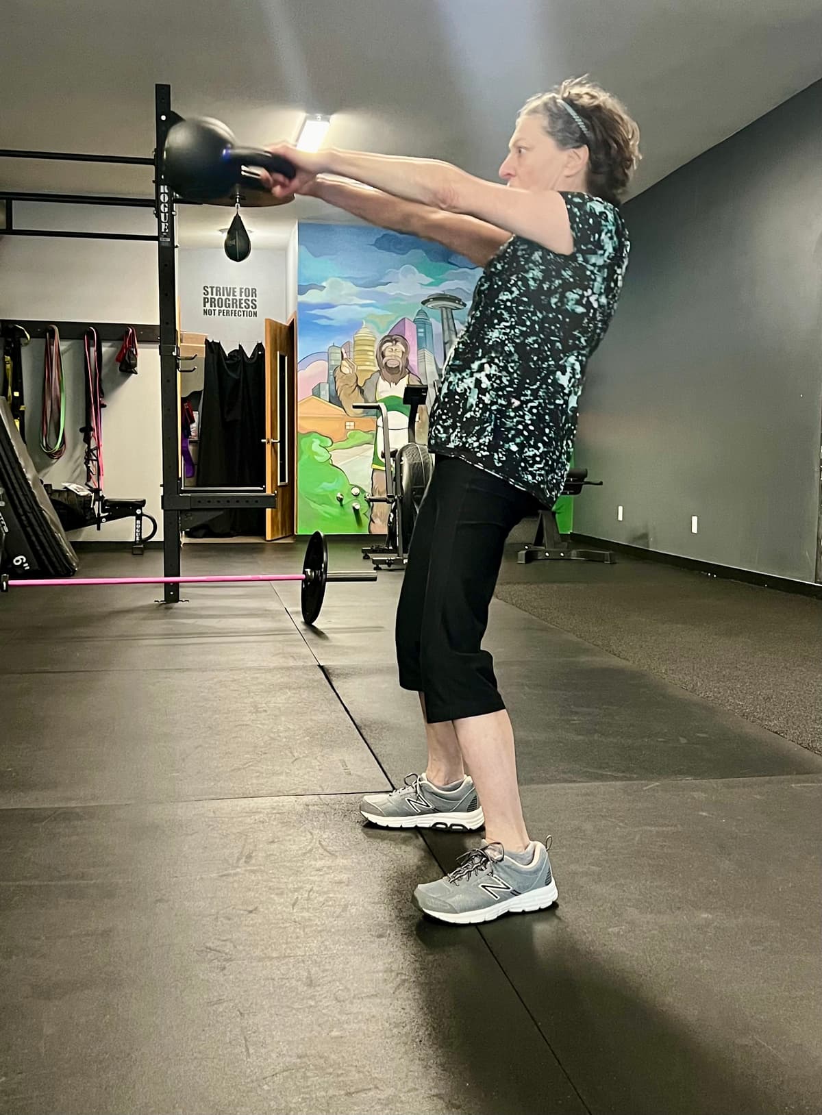 Member swinging a kettlebell at Seattle Muscle in Seattle, under the Strive For Progress sign